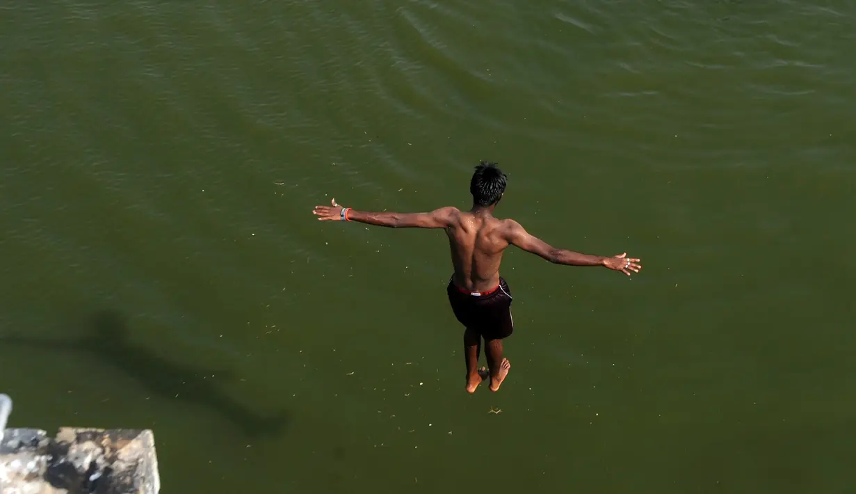 Seorang pemuda India melompat ke dalam sungai yang tercemar di pinggiran Chennai, India, Rabu (5/4). Sejumlah warga di India biasa mandi di sungai saat cuaca panas. (AFP PHOTO / ARUN SANKAR)