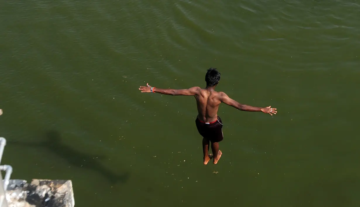 Seorang pemuda India melompat ke dalam sungai yang tercemar di pinggiran Chennai, India, Rabu (5/4). Sejumlah warga di India biasa mandi di sungai saat cuaca panas. (AFP PHOTO / ARUN SANKAR)