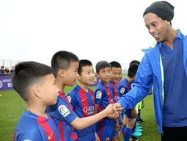 Pemain sepak bola asal Brasil, Ronaldinho bersalaman dengan pemain bola cilik di China (24/2). Mantan pemain klub Spanyol, Barcelona itu menghadiri peresmian berdirinya akademi sepak bola Barcelona di China. (Handout / Mission Hills / AFP)