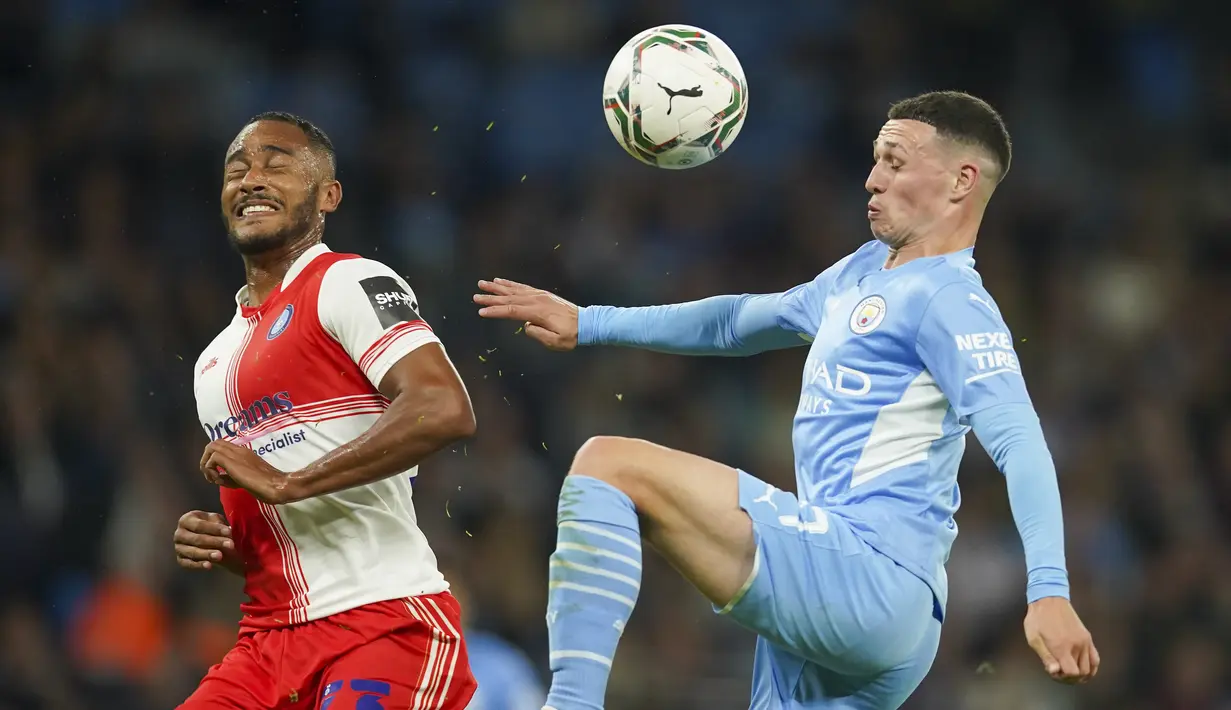 Gelandang Manchester City Phil Foden dan bek Wycombe Wanderers Jordan Obita berebut bola pada babak ketiga Piala Liga Inggris di Etihad Stadium, Rabu (22/9/2021) dini hari WIB. Manchester City menang telak 6-1 saat menjamu klub divisi tiga Wycombe Wanderers. (AP Photo/Dave Thompson)