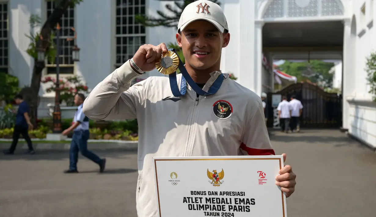 Peraih medali emas cabang olahraga angkat besi kelas -73kg putra Olimpiade Paris 2024, Rizki Juniansyah berfoto dengan medali yang diraihnya di Istana Merdeka, Jakarta, pada Kamis 15 Agustus 2024. (BAY ISMOYO/AFP)