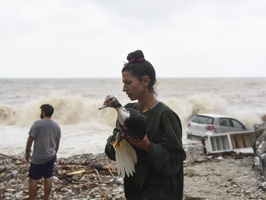 Seorang wanita menyelamatkan seekor burung di pantai setelah badai petir hebat, di desa Paliokastro, di pulau Kreta, Yunani, Sabtu (15/10/2022). Dilaporkan setidaknya satu orang tewas dan lainnya hilang setelah banjir bandang yang parah. (AP Photo/Harry Nakos)