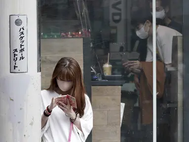 Seorang perempuan mengenakan masker melihat ponsel di distrik Shibuya, Tokyo, Kamis (30/9/2021). Jepang akan mencabut keadaan darurat COVID-19 di semua wilayah pada akhir September. (AP Photo/Eugene Hoshiko)