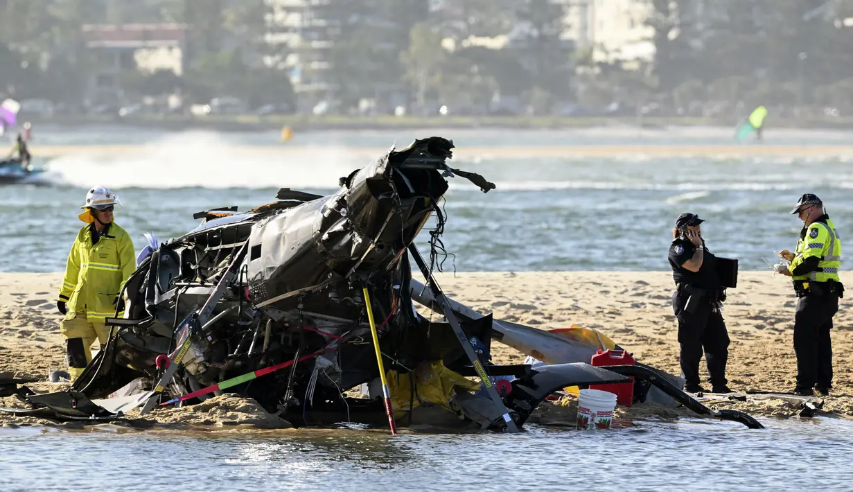 Petugas darurat memeriksa helikopter di lokasi tabrakan dekat Seaworld, di Gold Coast, Australia, Senin, 2 Januari 2023. Dua helikopter bertabrakan di udara menewaskan empat orang termasuk sepasang suami istri dari Inggris dalam kecelakaan yang menarik bantuan darurat dari pengunjung pantai selama musim panas. (Dave Hunt/AAP Image via AP)