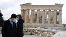 Pengunjung pertama yang mengenakan masker wajah berdiri di atas bukit Acropolis, dengan latar belakang kuil Parthenon di Athena, Senin (22/3/2021). Pemerintah Yunani membuka kembali Acropolis dan situs kuno lainnya secara nasional untuk memulai kembali musim pariwisata pada pertengahan Mei. (AP Phot