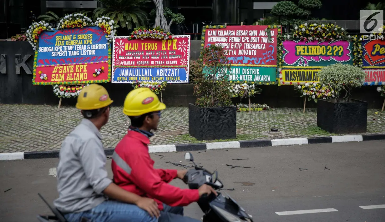 Pengendara melintas di depan karangan bunga berisi dukungan pada KPK di Gedung KPK, Jakarta, Senin (20/11). Karangan bunga tersebut sebagai bentuk dukungan masyarakat kepada KPK terhadap pemberantasan kasus korupsi e-KTP. (Liputan6.com/Faizal Fanani)