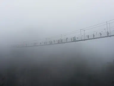 Wisatawan melewati jembatan gantung yang terbuat dari kaca di pegunungan Shinuizhai, Provinsi Hunan, Tiongkok, 6 Oktober 2015. Jembatan dengan panjang 300 m dan tinggi 180 m ini kembali dibuka setelah direnovasi untuk objek wisata. (AFP/Johannes Eisele)