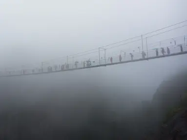 Wisatawan melewati jembatan gantung yang terbuat dari kaca di pegunungan Shinuizhai, Provinsi Hunan, Tiongkok, 6 Oktober 2015. Jembatan dengan panjang 300 m dan tinggi 180 m ini kembali dibuka setelah direnovasi untuk objek wisata. (AFP/Johannes Eisele)