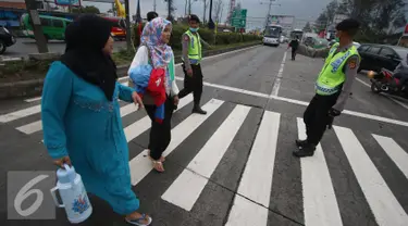 Petugas kepolisian membantu warga menyeberang jalan di Perempatan Cileunyi, Jawa Barat, Jumat (1/7). Mulai banyaknya kendaraan pemudik membuat petugas kepolisian membantu pejalan kaki yang ingin menyeberang. (Liputan6.com/Immanuel Antonius) 