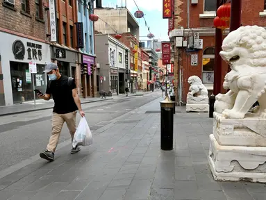 Seorang pria membawa belanjaannya di jalan sepi di Chinatown Melbourne, Australia, Selasa (19/10/2021). Melbourne bersiap mencabut aturan penguncian pekan ini setelah kota tersebut berada dalam enam pekan lockdown selama 262 hari atau hampir sembilan bulan sejak Maret 2020. (William WEST/AFP)