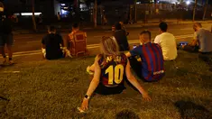 Seorang fans wanita mengenakan kaus replika nomor 10 Lionel Messi duduk di luar stadion Camp Nou di Barcelona (5/8/2021). Para fans berkumpul di depan stadion setelah Barcelona dan Lionel Messi sama-sama sepakat untuk resmi berpisah. (AP Photo/Joan Monfort)