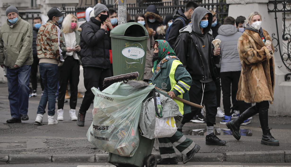 Petugas kota mendorong gerobak melewati antrean remaja di luar restoran untuk mendapatkan burger gratis selama acara promosi di Bucharest, Rumania, Senin (1/2/2021). Ratusan orang berkerumun demi burger gratis hingga polisi mendenda restoran karena tidak mematuhi protokol COVID-19. (AP/Vadim Ghirda)
