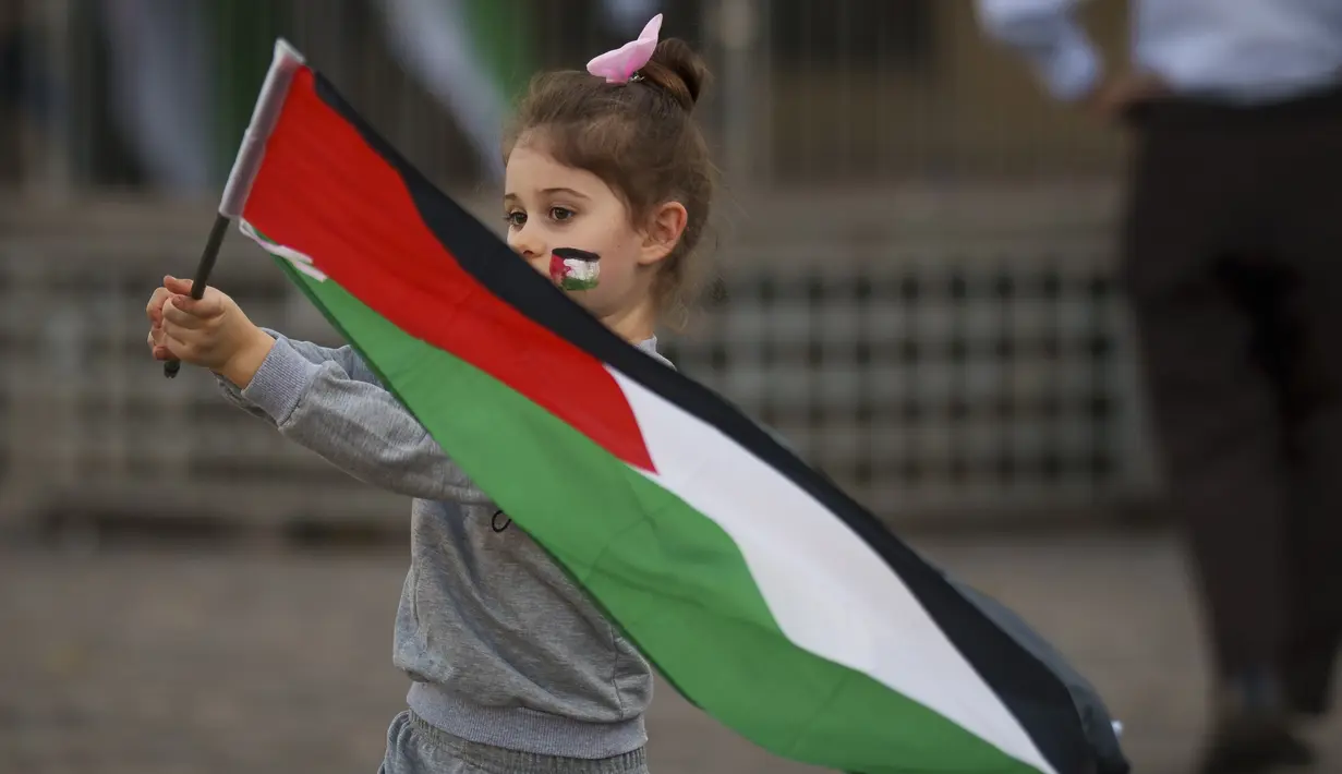 <p>Seorang anak kecil mengibarkan bendera Palestina sebelum unjuk rasa pro-Palestina yang diikuti oleh ratusan orang, di pusat kota Bucharest, Rumania, Sabtu, 21 Oktober 2023. (AP Photo/Andreea Alexandru)</p>