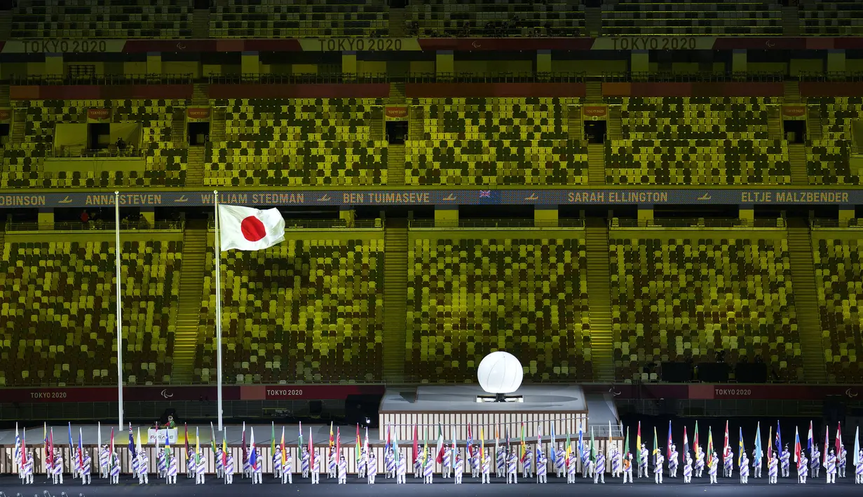 Para asisten atlet parade memegang bendera negara yang bertanding pada upacara pembukaan Paralimpiade Tokyo 2020 di Tokyo, Jepang, Selasa, 24 Agustus 2021. (OIS via AP Photo/Bob Martin)