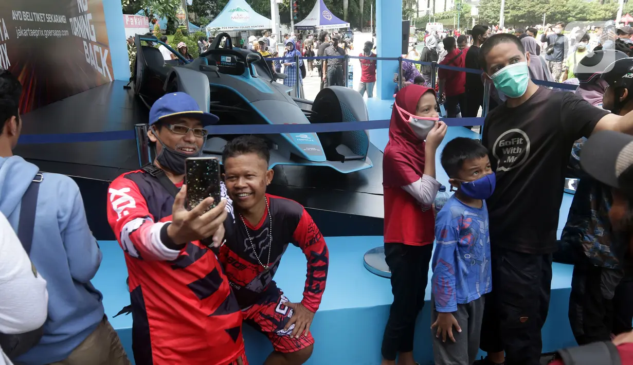 Warga berfoto dengan latar replika mobil Formula E yang dipamerkan di Kawasan Bundaran Hotel Indonesia, Jakarta, Minggu (29/5/2022). Replika mobil balap ramah lingkungan ini dipamerkan untuk mengkampanyekan perhelatan Formula E yang akan digelar 4 Juni mendatang. (Liputan6.com/Helmi Fithriansyah)