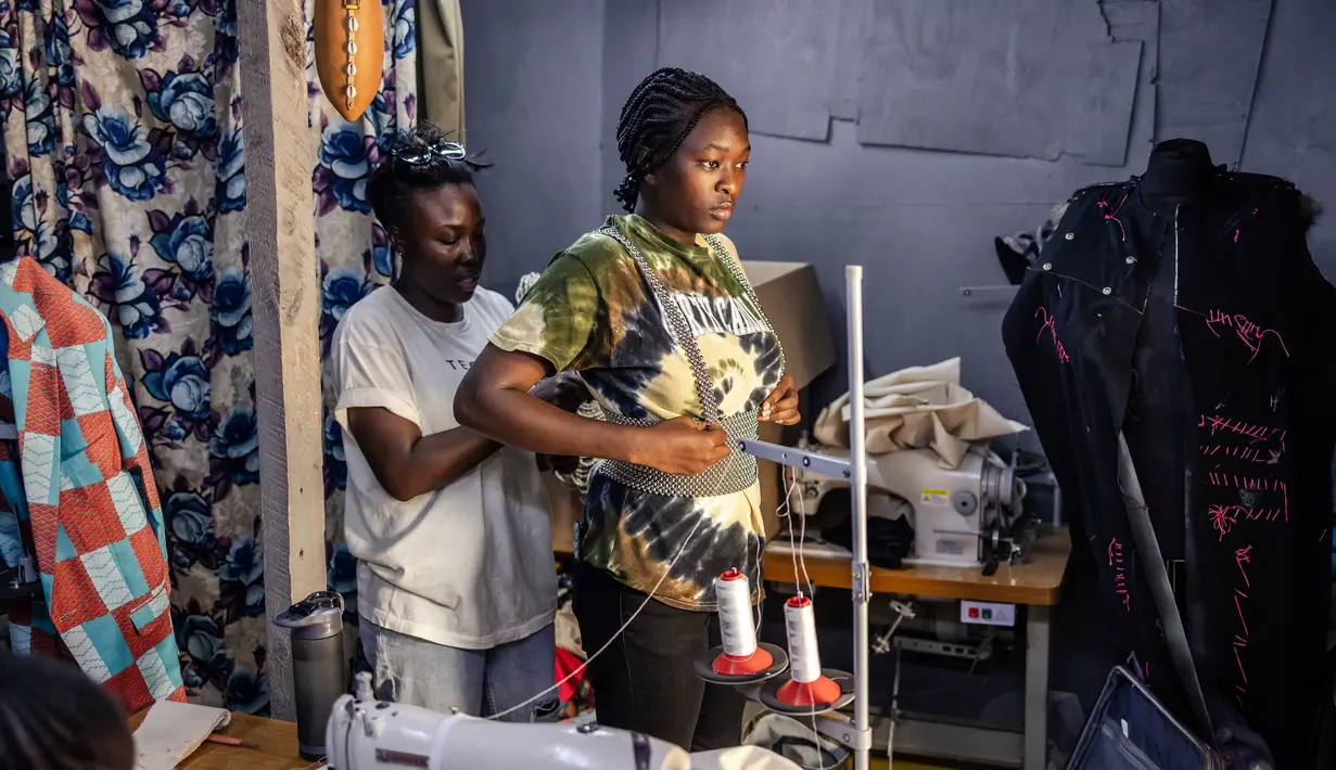 Seorang perancang busana menyesuaikan kreasi pada model amatir selama sesi fitting di sebuah studio mode di pemukiman informal Kibera di Nairobi, pada tanggal 20 September 2023 menjelang Kibera Fashion Week. (LUIS TATO/AFP)
