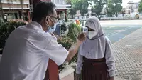 Guru memeriksa suhu tubuh murid kelas 1 sebelum mengikuti PTM Terbatas di SDN Malaka Jaya 07 Pagi, Klender, Jakarta, Senin (30/8/2021). Kembali digelarnya PTM hari ini disambut antusias murid, terutama kelas 1 SD yang baru pertama kali belajar langsung di ruang kelas. (merdeka.com/Iqbal S. Nugroho)