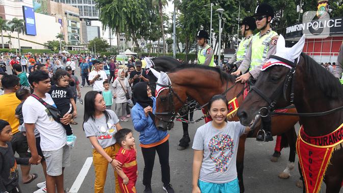 Warga berpose disamping polisi berkuda yang sedang berpatroli di car free day  di Bundaran Hotel Indonesia, Jakarta Pusat, Minggu (12/1/2020). Kehadiran polisi berkuda ini sebagai bentuk dukungan terhadap program CFD pemerintah. (Liputan6.com/Angga Yuniar)
