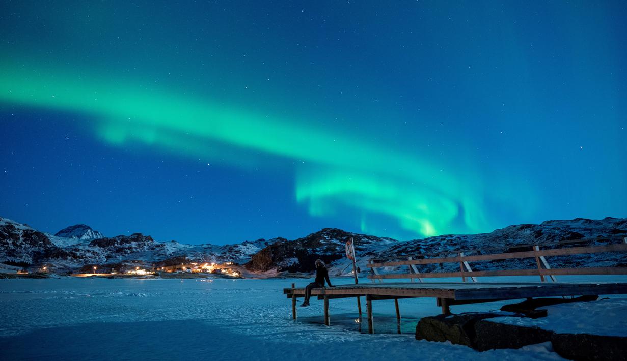 Seorang wanita duduk di dermaga untuk menonton Aurora Borealis atau Northern Lights di di Kepulauan Lofoten, Bostad, lingkaran Arktik, Norwegia, Sabtu (3/3). Cahaya Aurora biasa terlihat di sekitar daerah Kutub Utara dan Selatan. (Olivier MORIN/AFP)