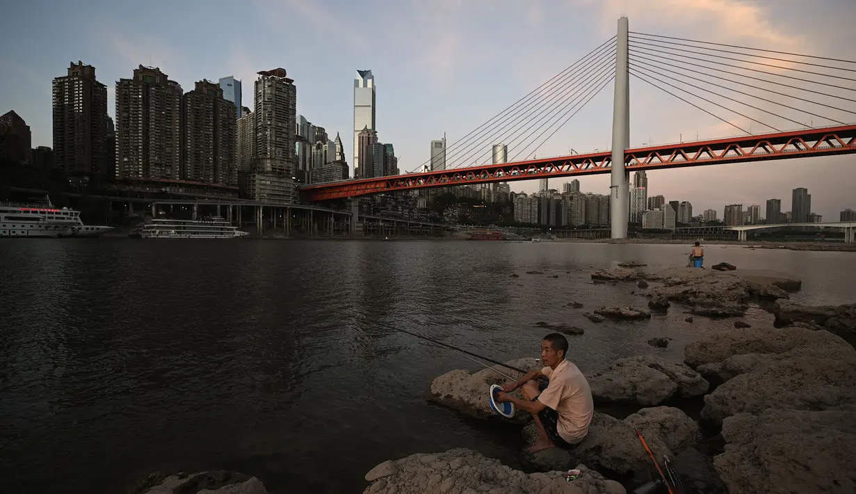 Pemancing memancing di Sungai Jialing, anak Sungai Yangtze, di Kota Chongqing, China, Rabu (24/8/2022). Yangtze adalah sungai terbesar ketiga di dunia, menyediakan air minum untuk lebih dari 400 juta orang China, dan merupakan jalur air paling vital bagi perekonomian China. (Noel Celis/AFP)