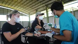 Dua warga negara asing (WNA) menjalani pemeriksaan tekanan darah sebelum menerima vaksin virus corona COVID-19 AstraZeneca di klinik vaksinasi massal darurat di Denpasar, Bali, Selasa (6/7/2021). Indonesia tengah memerangi gelombang infeksi baru yang belum pernah terjadi sebelumnya. (SONNY TUMBELAKA