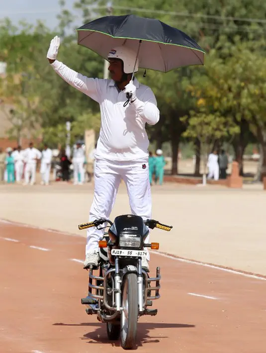 Anggota polisi India berdiri di atas motor sambil memegang payung saat beratraksi mengikuti parade di Pusat Pelatihan Polisi Rajasthan di Jodhpur, India, Jumat (24/4/2015).(AFP FOTO)