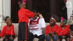 Presiden Joko Widodo atau Jokowi mendapatkan hadiah dari perwakilan anak-anak sekolah dasar Papua di Istana Merdeka, Jakarta, Jumat (11/10/2019). Pertemuan Jokowi dengan perwakilan anak-anak SD dari Papua digelar dalam suasana santai di beranda belakang Istana Merdeka. (Liputan6.com/Angga Yuniar)