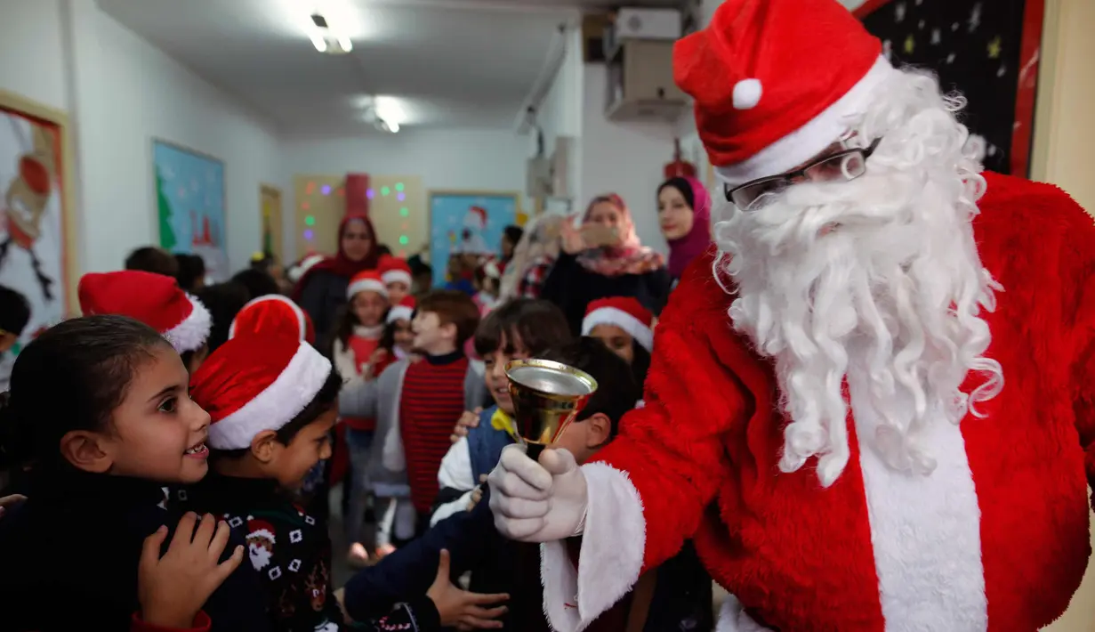 Seorang pria berpakaian seperti Santa Claus menyambut kedatangan anak-anak  saat perayaan menyambut Hari Natal di Sekolah Amerika di Kota Gaza (20/12).  (AFP Photo/Mohammed Abed)