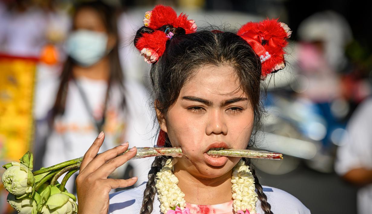 Seorang wanita menusuk pipinya dengan batang daun saat mengikuti prosesi perayaan Festival Vegetarian tahunan di Phuket, Thailand, Kamis (3/10/2019). Festival menyiksa diri ini dipercaya bagi warga Phuket akan mendapat kesehatan dan ketenangan pikiran. (AFP Photo/Mladen Antonov)