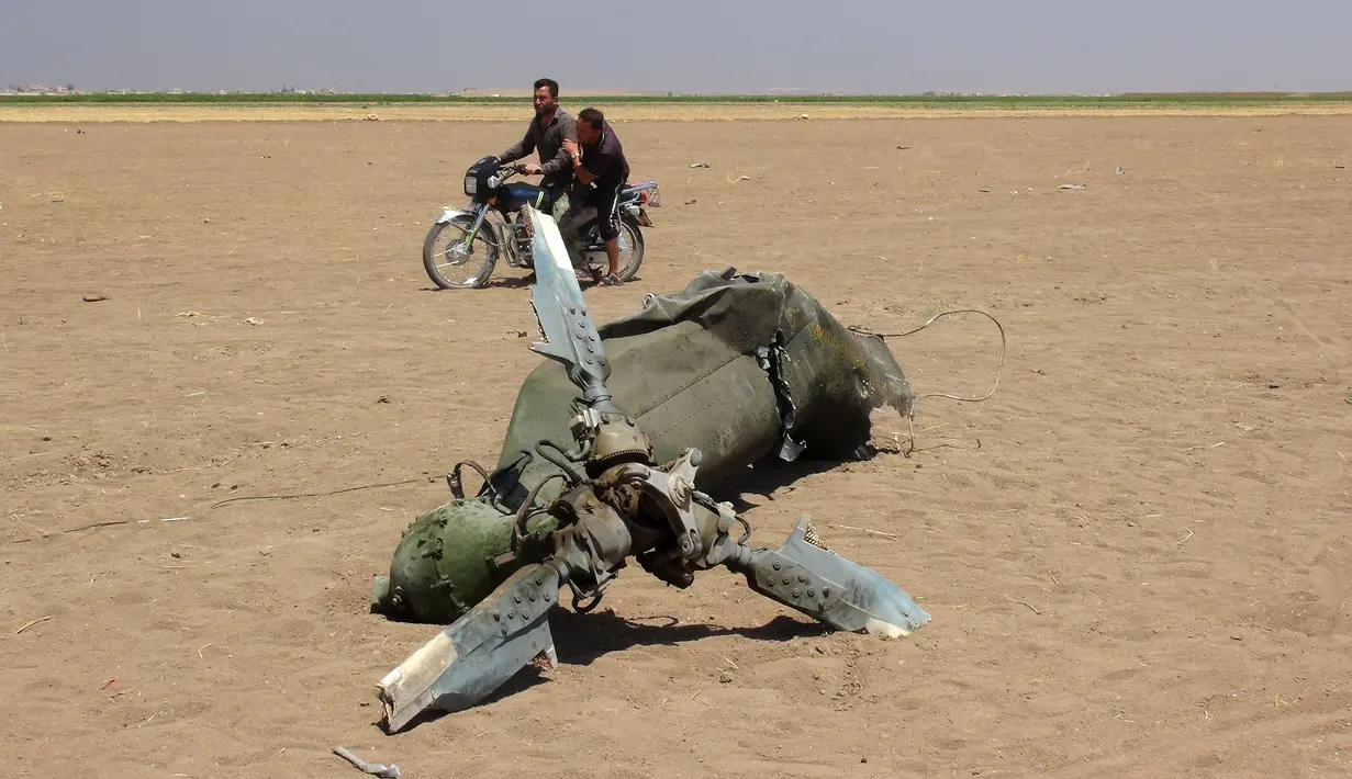 Dua pria yang mengendarai motor melewati reruntuhan helikopter Rusia yang ditembak jatuh di wilayah Idlib, Suriah, Senin (1/8). Menurut laporan, helikopter itu dalam perjalanan kembali setelah membawa bantuan kemanusiaan ke Aleppo. (Mohamed al-Bakour/AFP)
