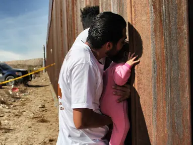 Seorang pria sambil menggendong bayi melepas rindu dengan kerabat dalam acara "Keep our dream alive" di dinding perbatasan antara Meksiko dan Amerika Serikat di Ciudad Juarez, negara bagian Chihuahua, 10 Desember 2017. (Herika MARTINEZ/AFP)