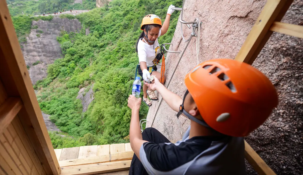 Seorang pemanjat tebing membeli air mineral di toko serba ada yang menempel di dinding tebing di Pingjiang di provinsi Hunan, China (25/4). (AFP Photo/China Out)