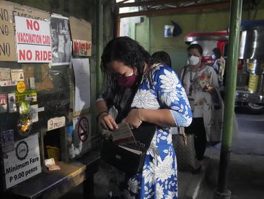 Seorang wanita memegang kartu vaksinasinya sebelum menaiki jip penumpang di sebuah terminal di kota Quezon, Senin (17/1/2022). Pemerintah Filipina melarang orang yang belum menerima vaksin COVID-19 untuk naik transportasi umum di ibu kota Manila mulai Senin ini. (AP Photo/Aaron Favila)