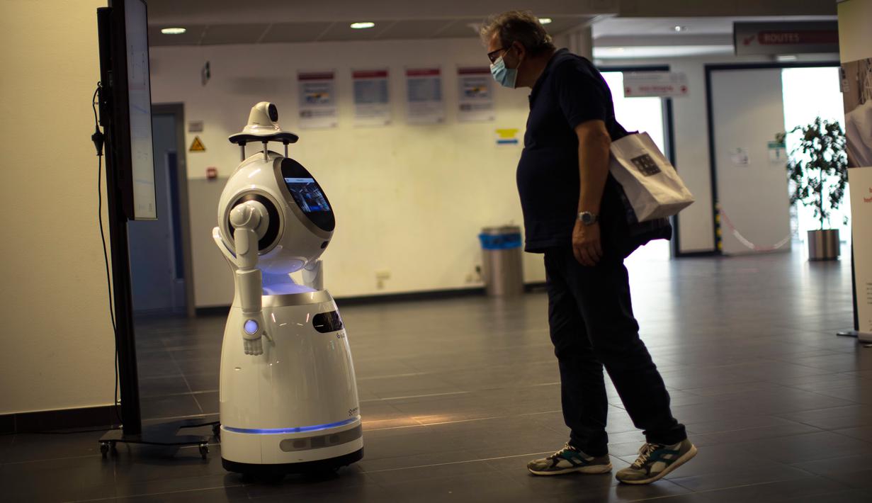 Seorang pria melihat pada robot yang dapat mendeteksi suhu dan masker di rumah sakit Universitas UZA di Antwerpen, Belgia pada 29 Mei 2020. Perusahaan Belgia, ZoraBots, menguji robot yang disebut CRUZR tersebut sebelum digunakan dalam beberapa minggu mendatang. (AP/Francisco Seco)