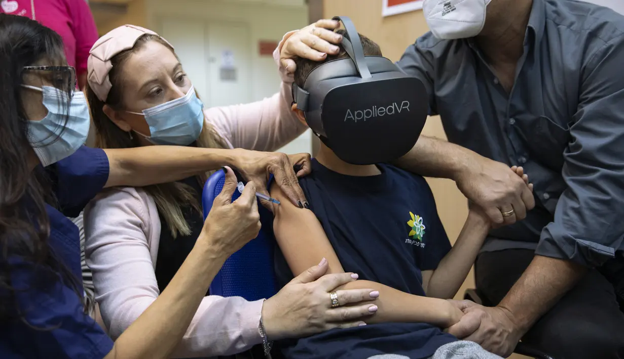 Seorang anak, Rafael Peled (8) melihat melalui kacamata realitas virtual VR saat menerima vaksin COVID-19 Pfizer-BioNTech di Rumah Sakit Sheba Tel Hashomer di Ramat Gan, Senin (22/11/2021). Israel mulai menyuntikkan vaksin Covid-19 pada anak usia 5 hingga 11 tahun. (AP Photo/Oded Balilty)