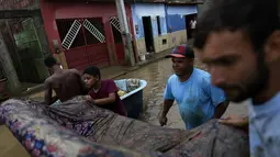 Warga membawa sofa saat membersihkan rumah mereka yang terendam banjir di Itapetinga, negara bagian Bahia, Brasil, Selasa (28/12/2021). Dua bendungan jebol pada Minggu (26/12) di timur laut Brasil, mengancam banjir yang lebih parah di wilayah yang diguyur hujan. (AP/Raphael Muller)