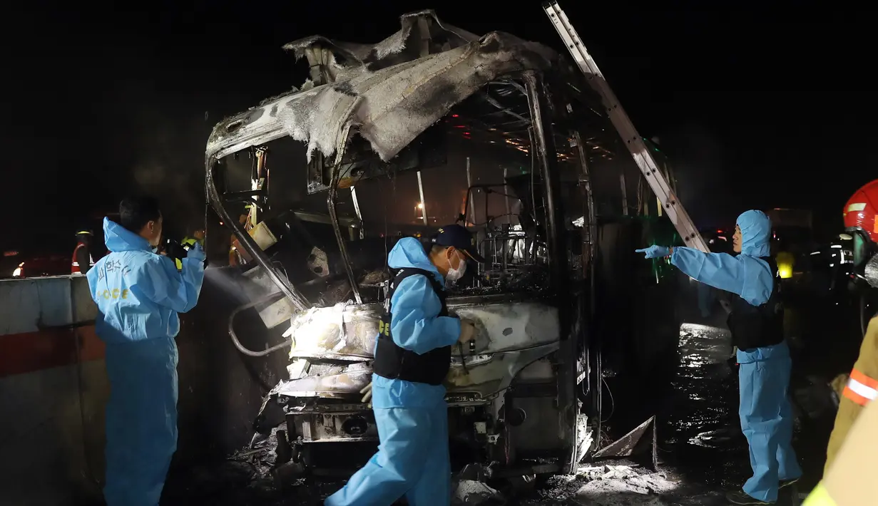 Petugas melakukan penyelidikan di lokasi terbakarnya bus pariwisata di Gyeongbu Expressway, tenggara Kota Ulsan, Korea Selatan, Jumat (14/10). Bus berisi 20 wisatawan lokal itu terbakar setelah tergelincir dan menabrak pembatas jalan tol. (Yonhap/AFP)