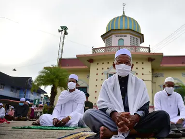 Pria-pria Muslim mengenakan masker dan duduk dengan menjaga jarak untuk melaksanakan salat berjemaah pada Idul Fitri yang menandai akhir bulan suci Ramadhandi halaman masjid Yakaniah di Narathiwat, provinsi selatan Thailand, 24 Mei 2020. (Photo by Madaree TOHLALA / AFP)