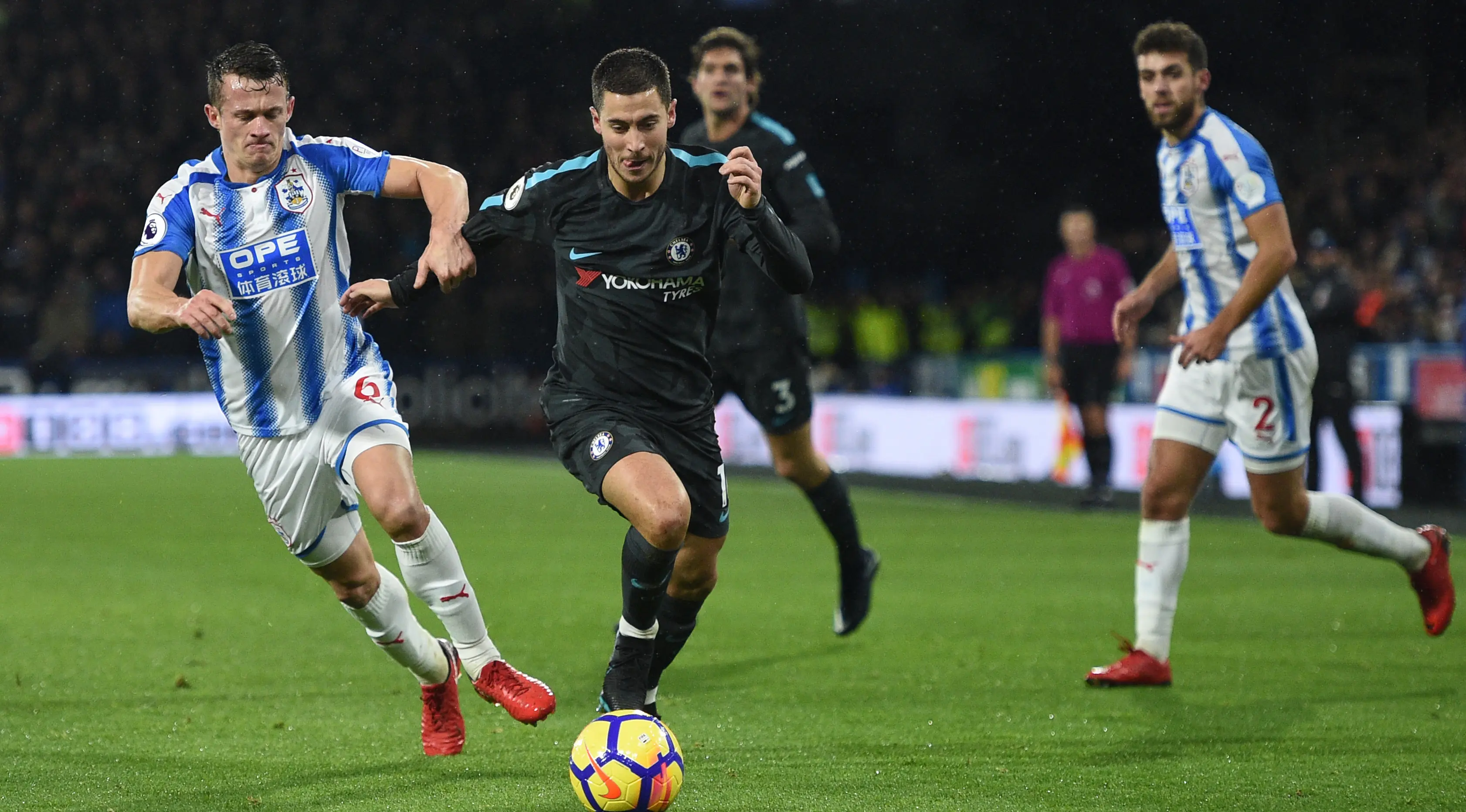 Pemain Huddersfield Town, Jonathan Hogg berebut bola dengan pemain Chelsea, Eden Hazard dalam lanjutan pertandingan Premier League di Stadion The John Smith's, Selasa (12/12). Chelsea berhasil memenangkan pertandingan dengan skor 3-1. (Oli SCARFF / AFP)