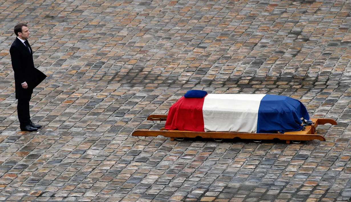 Presiden Prancis Emmanuel Macron  berdiri di dekat peti Letnan Kolonel Arnaud Beltrame dalam upacara nasional di Hotel des Invalides, Paris, Rabu (28/3). Macron memberikan penghargaan perwira tertinggi bagi Beltrame, Legiun d'Honneur. (AP/Christophe Ena)