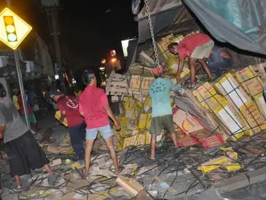 Sejumlah warga membantu mengangkat keramik saat truk gandeng terguling di jalur pantura, Tegal, Jateng, Jumat (30/3) malam. Truk pengangkut keramik terguling karena as roda patah mengakibatkan dua pengendara sepeda motor cedera tertimpa truk dan pantura sempat macet selama 5 jam. (Antara)