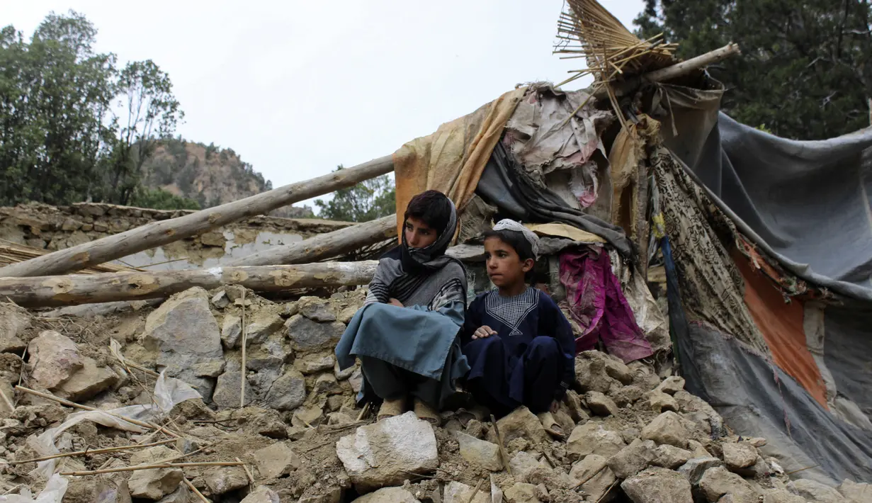 Duan anak laki-laki berada dekat rumah mereka yang rusak dalam gempa bumi di Distrik Spera, bagian barat daya Provinsi Khost, Afghanistan, 22 Juni 2022. Petugas PBB telah berusaha membantu situasi, namun upaya evakuasi terhambat oleh hujan deras. (AP Photo)