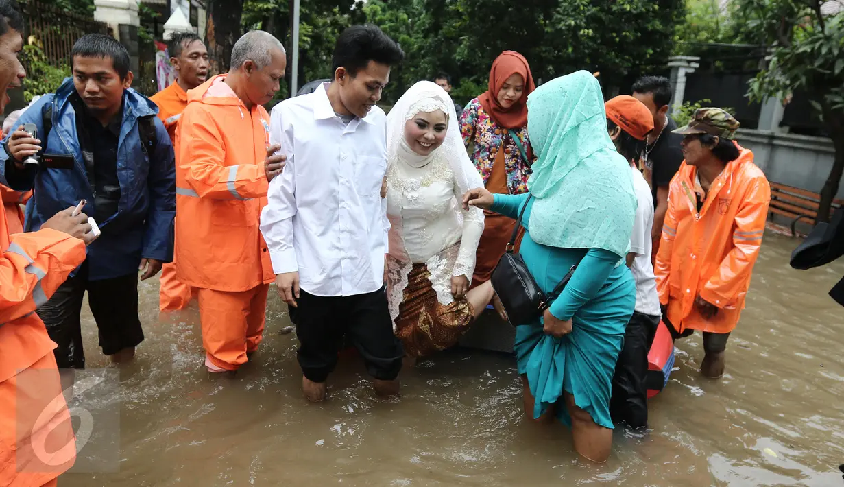 Keluarga pengantin dan pengantin Mansur dan Maya di evakuasi pasukan orange seusai melakukan akad nikah di KUA Mampang Prapatan, Jakarta, Selasa (21/2). Walaupun banjir sepasang pengantin ini tetap melakukan akad nikah. (Liputan6.com/Herman Zakharia)