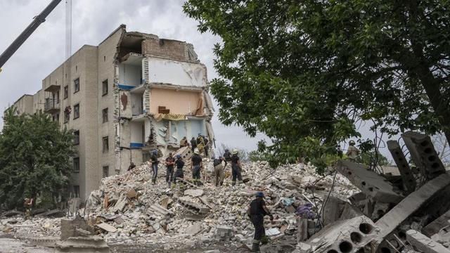 Petugas penyelamat berdiri di atas puing-puing di tempat kejadian setelah serangan rudal Rusia mengenai blok apartemen perumahan, di Chasiv Yar, wilayah Donetsk, Ukraina timur, Minggu, 10 Juli 2022. (AP Photo/Nariman El-Mofty)