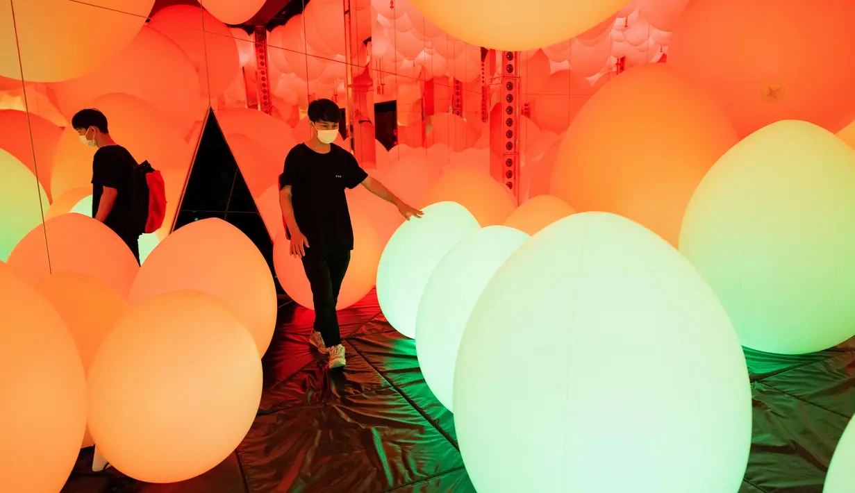 Seorang anggota staf berjalan melalui instalasi digital interaktif bernama "Typhoon Balls and Weightless Forest of Resonating Life" selama pratinjau media "teamLab Forest" di gedung hiburan BOSS E・ZO FUKUOKA di Fukuoka, Jepang, Jumat (16/7/2021). (YUKI IWAMURA/AFP)