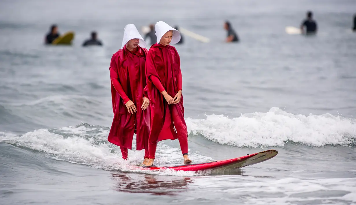 Erik dan April berselancar menggunakan kostum karakter dari The Handmade's Tale di Newport Beach, California, 28 Oktober 2017. Acara ini untuk merayakan Halloween yang jatuh pada tanggal 31 Oktober. (Paul Rodriguez/The Orange County Register via AP)