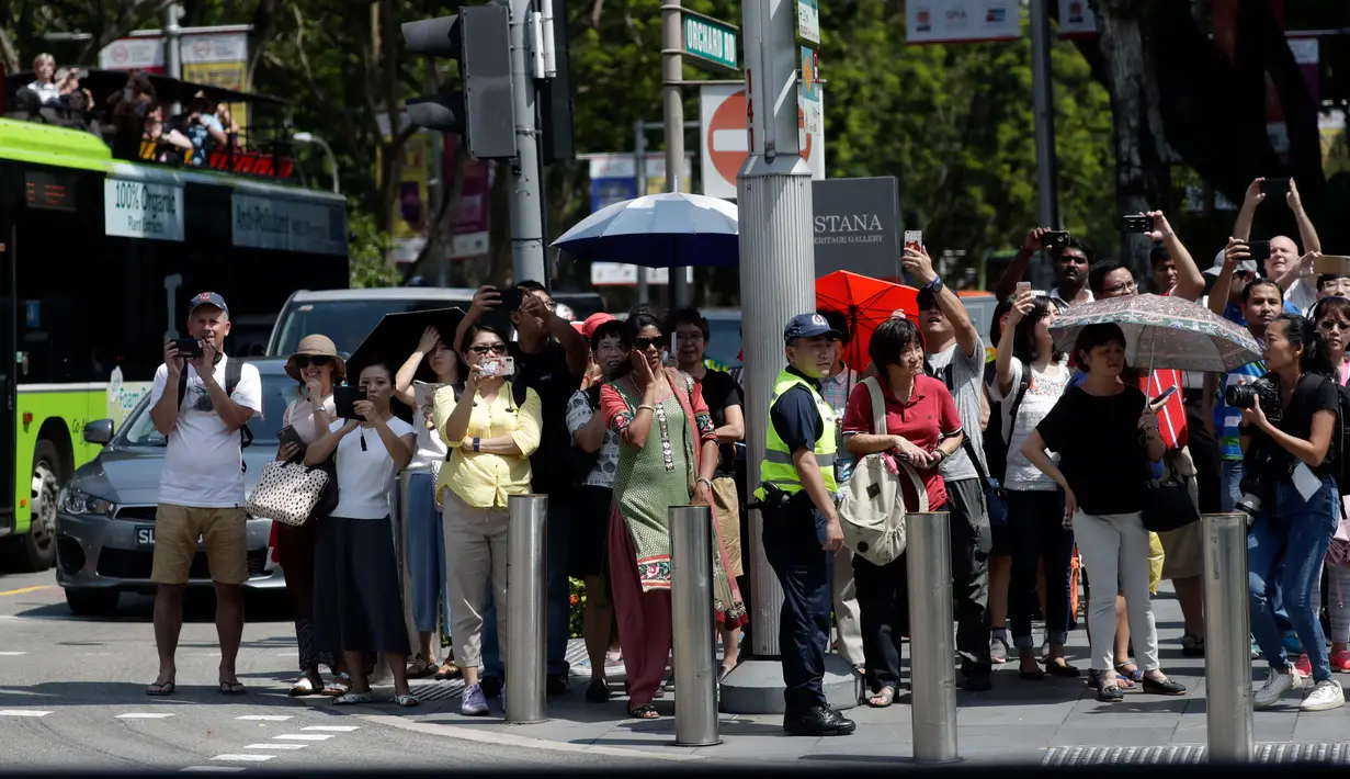 Kerumunan penduduk berjejer di trotar yang diberi pembatas di sepanjang jalan Orchard Road, Singapura, Senin (11/6). Tampak mereka menunggu kedatangan Presiden Amerika Serikat, Donald Trump. (AP/Joseph Nair)