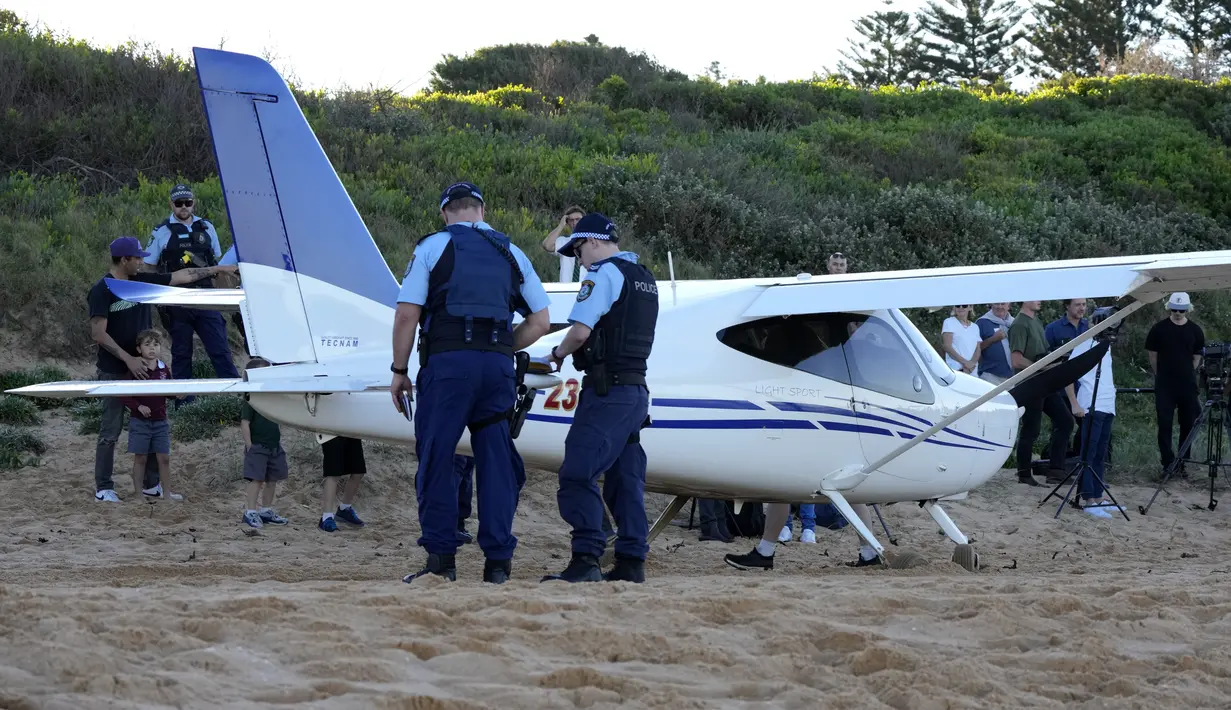 Polisi berdiri di dekat sebuah pesawat ringan yang melakukan pendaratan darurat di sebuah pantai di Sydney, Rabu (26/5/2021). Pesawat kategori rekreasi itu mendarat selamat di pantai Sydney dengan tiga orang di dalamnya termasuk seorang bayi setelah mengalami kerusakan mesin. (AP Photo/Mark Baker)