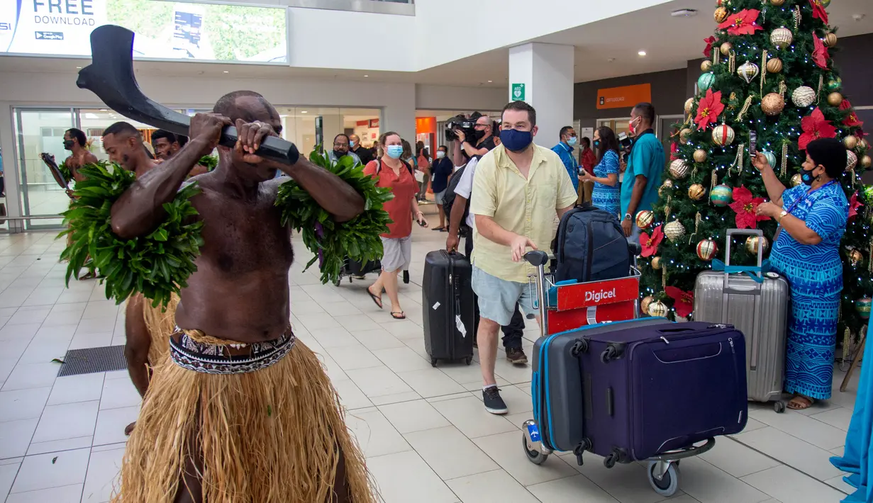 Penari tradisional dengan rok rumput menyambut wisatawan di Nadi, Fiji, Rabu (1/12/2021). Fiji membuka perbatasannya untuk pelancong internasional pertama kalinya sejak pandemi Covid-19 melanda dunia dan menghancurkan ekonominya yang bergantung pada pariwisata. (Leon LORD/AFP)