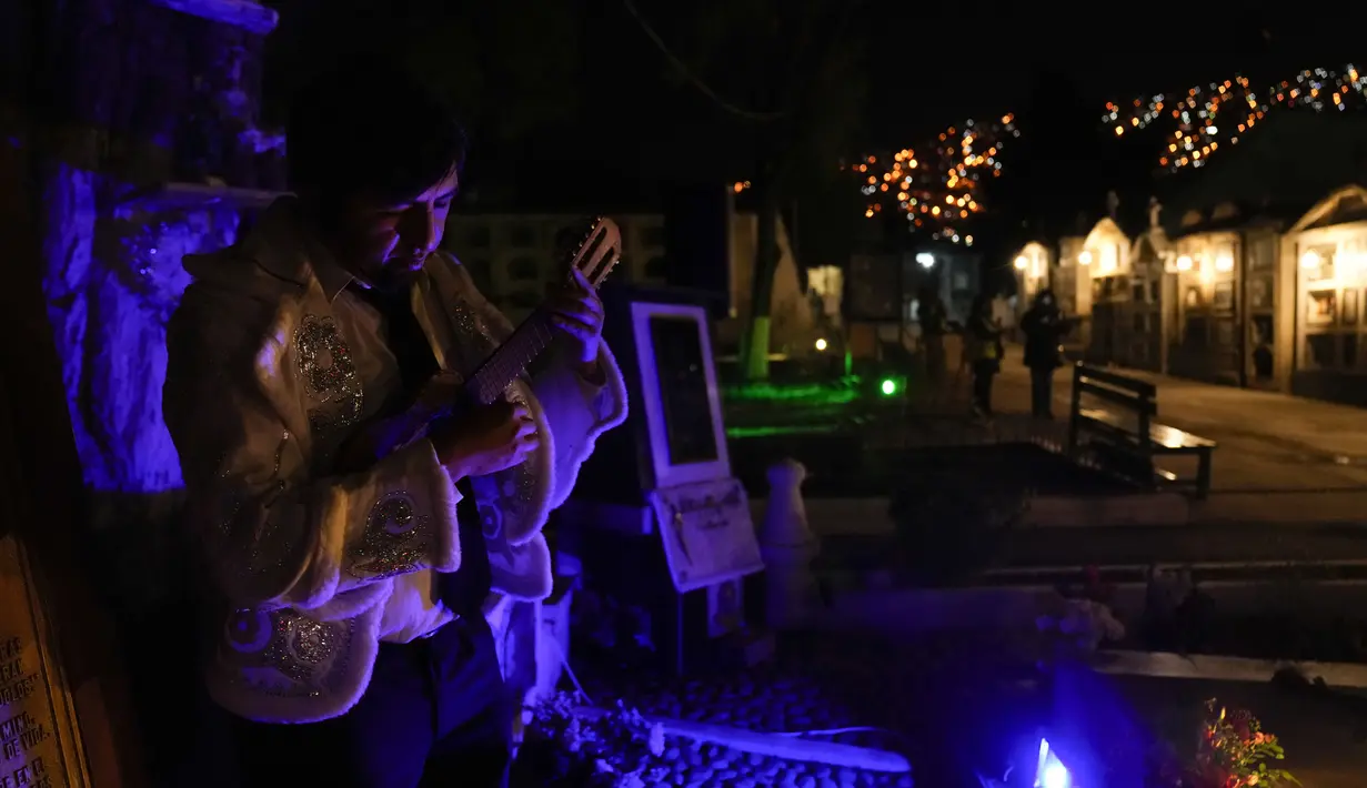 Seorang musisi memetik instrumennya selama tur Pemakaman Umum di La Paz, Bolivia, 29 Oktober 2021. Warga mengunjungi pemakaman pada perayaan Hari Kematian untuk menggambarkan kehidupan musisi dan komposer terkenal Bolivia yang telah dimakamkan di kuburan. (AP Photo/Juan Karita)